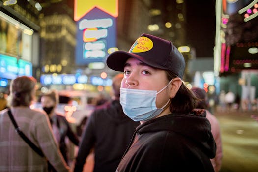 A young adult in Times Square at night wearing a mask and hat, capturing urban nightlife.